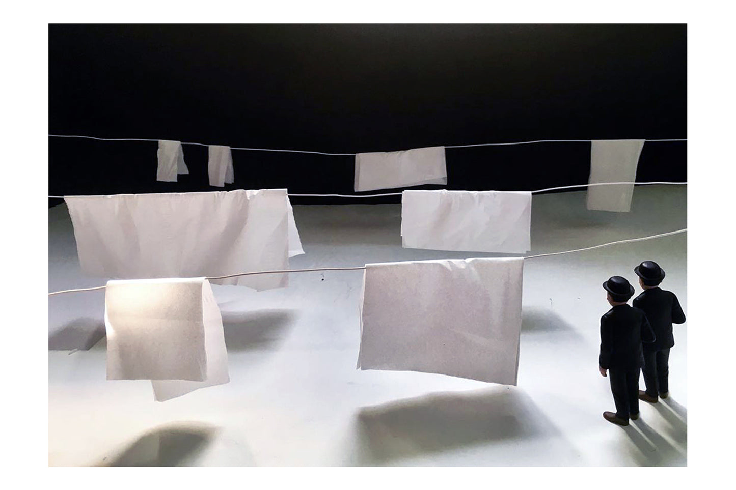 There is three clothesline and white bedsheets on them. two men with black clothes are in foreground looking bedsheets.