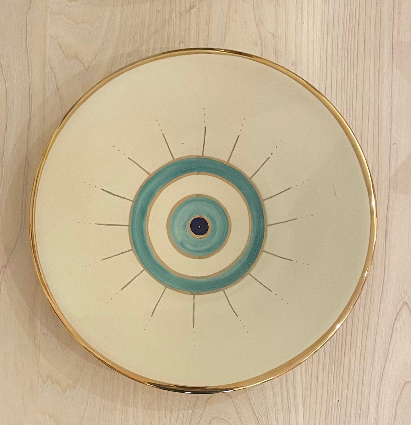 Beige ceramic plate with golden edge and eye design on the center.