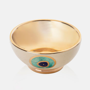 A ceramic bowl with golden edge and Eye design on it. inside of the bowl is golden and outside of it is beige with eye design.