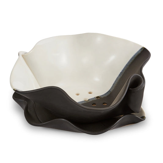 Irregular black and white ceramic bowl with holes on the bottom.