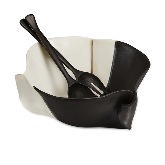 Irregular black and beige ceramic bowl with black wooden spoon and fork.
