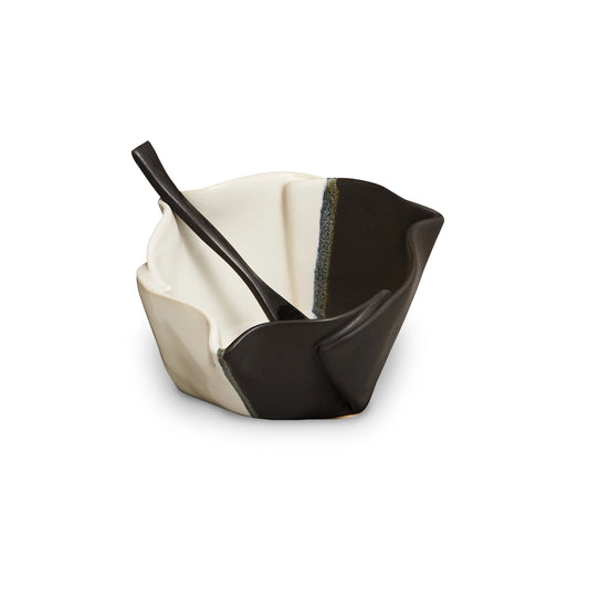 Irregular black and beige ceramic bowl with black wooden spoon.
