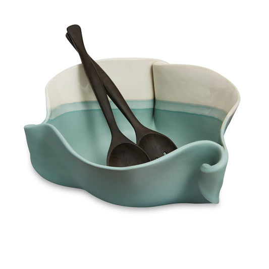 Irregular green and beige ceramic bowl with black wooden spoon and fork.
