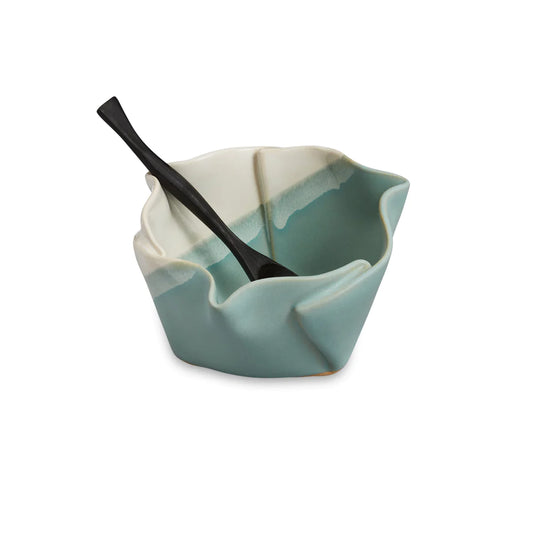 Irregular green and beige ceramic bowl with black wooden spoon.