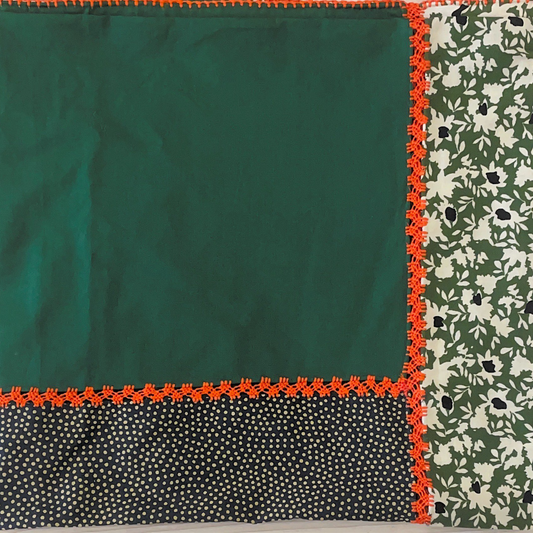 A tablecloth made of several piece of fabric with different patterns in green tonnage and orange embroidery on edges .