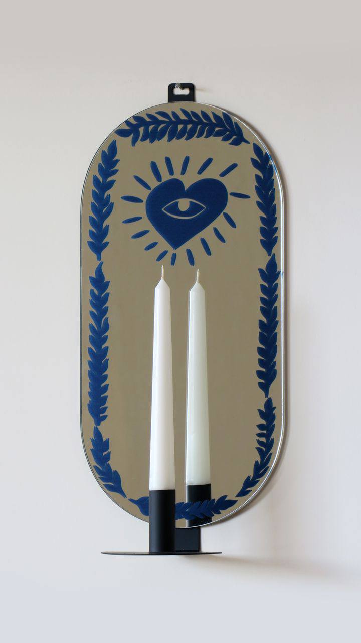 Oval mirror with digital print, and a metal candlestick in front of the mirror.