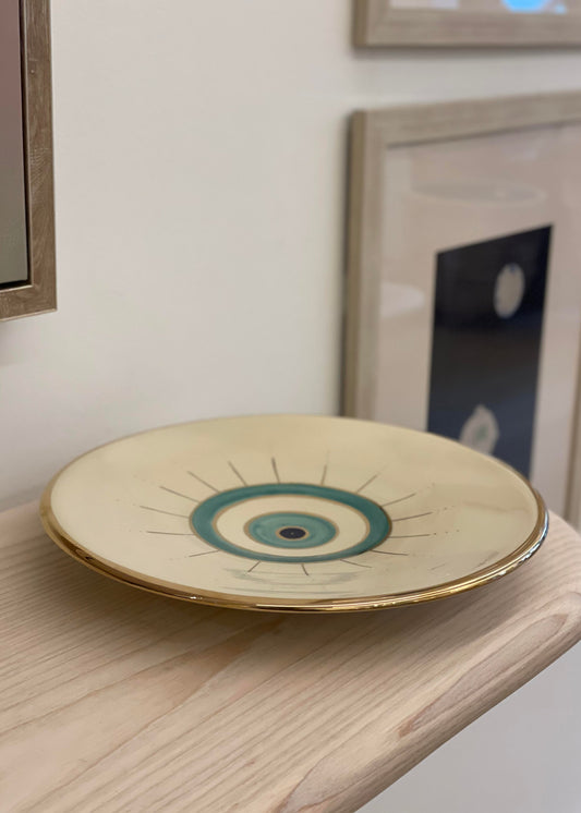 Beige ceramic plate with golden edge and eye design on the center.