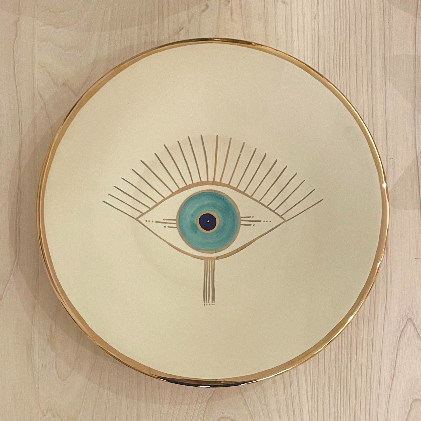 Beige ceramic plate with golden edge and eye design on the center.