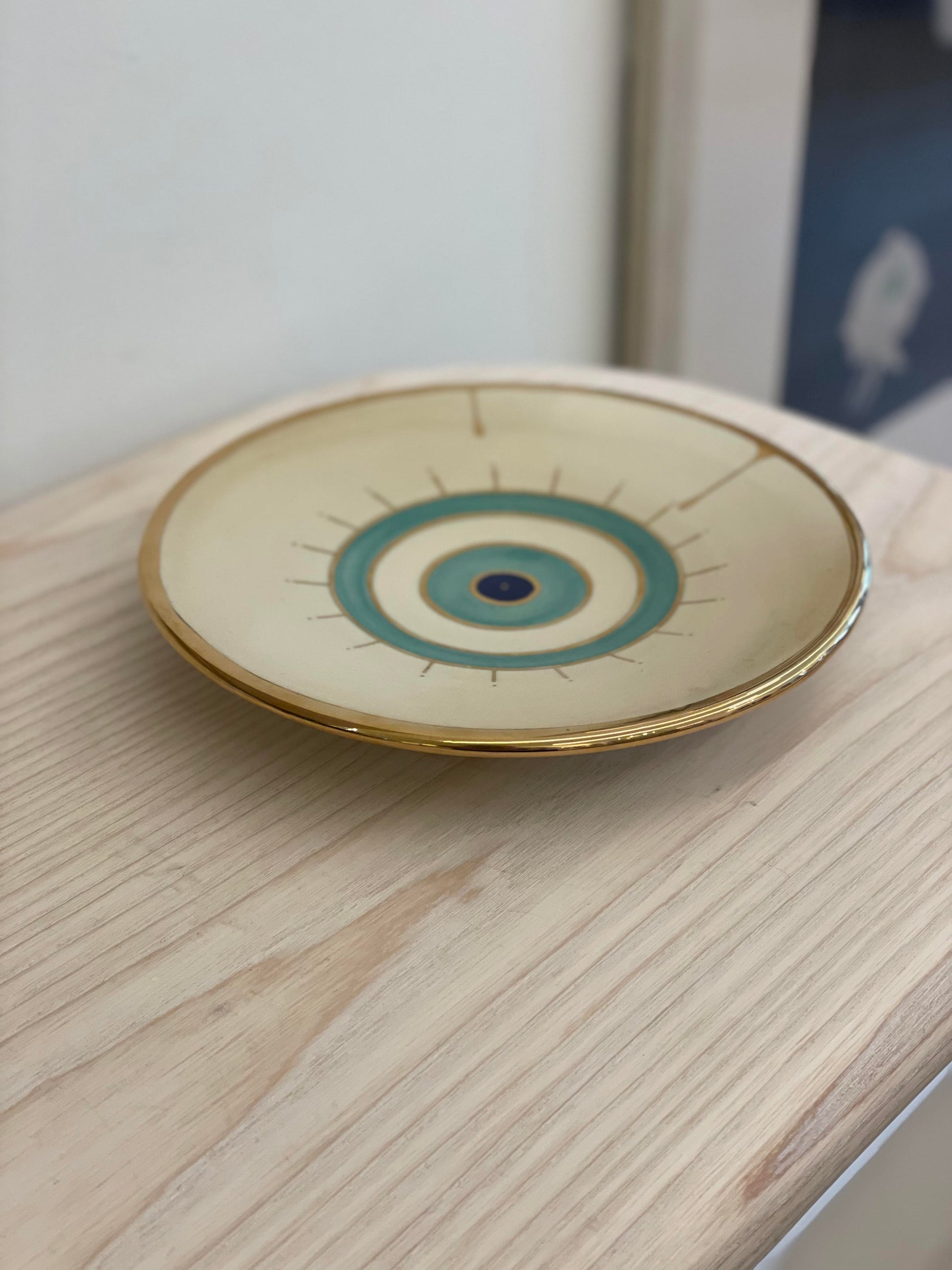 Beige ceramic plate with golden edge and eye design on the center.