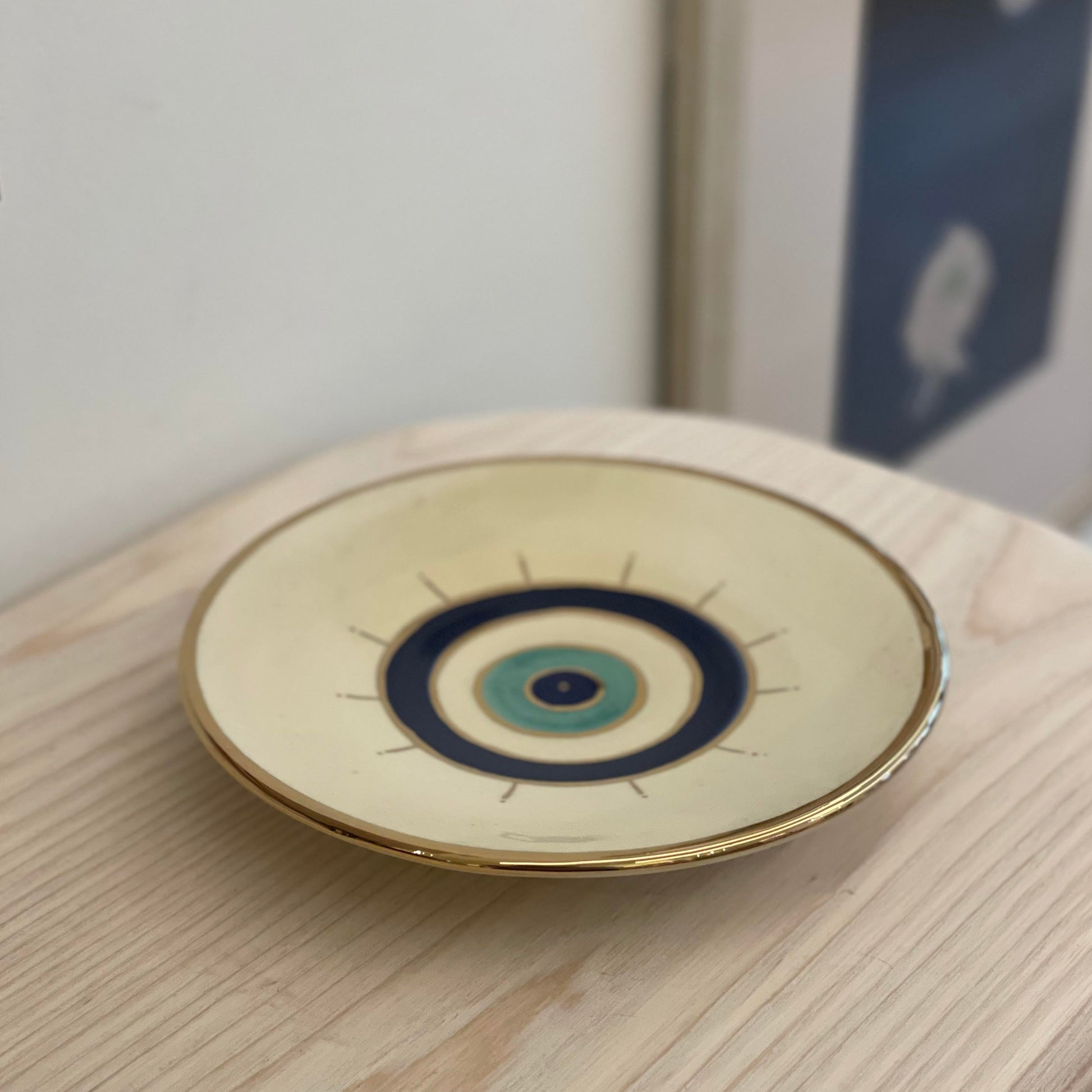 Beige ceramic plate with golden edge and eye design on the center.